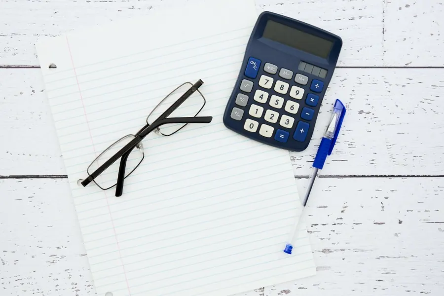A notebook, reading glasses and a calculator on a desk